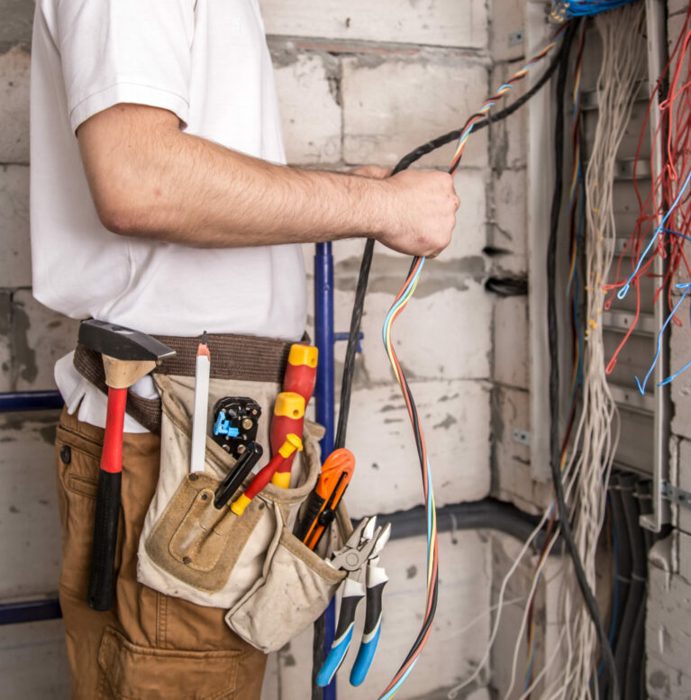 Electrician working near the Board with wires. Installation and connection of electrics. Professional with tools in hand.